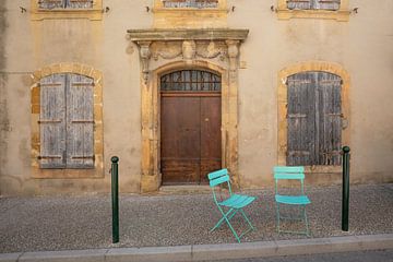 Gele muur met deur, twee ramen en twee fel blauwe stoeltjes