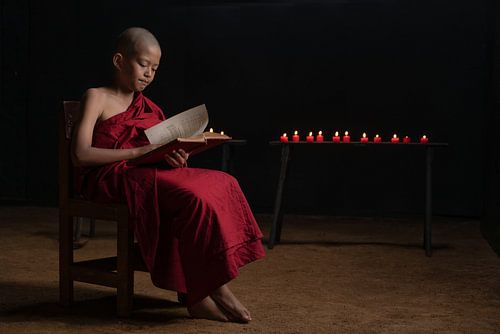 A young monk reading by candlelight