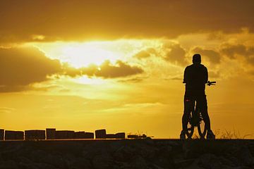 Silhouet van eenzame fietser die geniet van zonsondergang boven de Westerschelde.