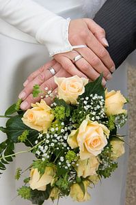 Mains d'un couple de mariés sur le bouquet de la mariée