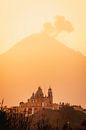 Kerk en vulkaan met wolken tijdens de warme, oranje, zonsopkomst in Mexico van Maartje Hensen thumbnail