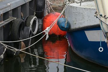 Orange buoy with reflection in the water and detail of a fishing boat tied at the dock in the port,  by Maren Winter