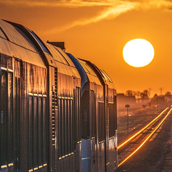 Un train s'approche d'une gare au coucher du soleil et les voies s'illuminent. par Harrie Muis