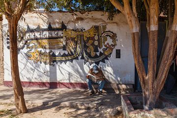 Street scene in Nazca, Peru. Reading man under trees in front of a mural by Martin Stevens