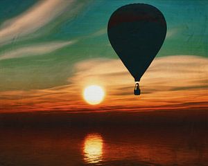 A hot air balloon travels over the sea during sunset