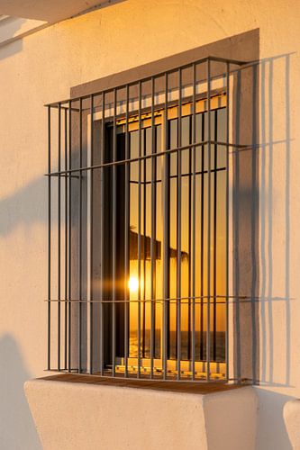 Zonsondergang weerspiegeld in een raam van een witte gevel. Rota, Costa de la Lutz, Cádiz, Andalusië, Spanje.