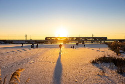 Schaatsen op de by-pass bij Kampen met een trein en een zonsondergang boven de Hanzelijn