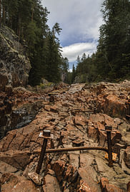 Schwedische Natur – Vertikaler Fotodruck der historischen Holzflößerei in der Brattfallet-Schlucht von Dylan Winter Visuals