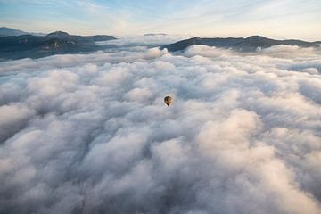 A hot air balloon flies over a sea of ​​clouds during sunrise. by Carlos Charlez