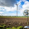 Zilveren huishoudventilator staand op een veld voor een windturbine van Maren Winter
