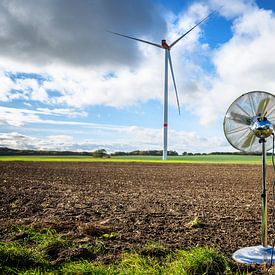 Zilveren huishoudventilator staand op een veld voor een windturbine van Maren Winter