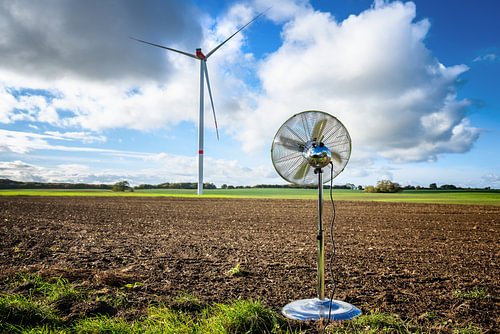 Silberner Haushaltsventilator, der auf einem Feld vor einer Windkraftanlage steht