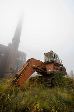 Verlaten graafmachine en fabriek met mist