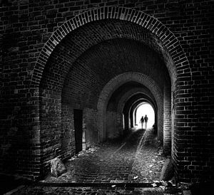 zwei Personen laufen als Silhouetten wie ein Paar durch einen alten dunklen Backsteintunnel zum Lich
