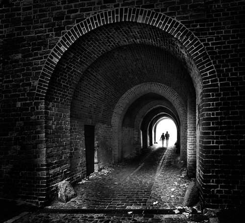 zwei Personen laufen als Silhouetten wie ein Paar durch einen alten dunklen Backsteintunnel zum Lich