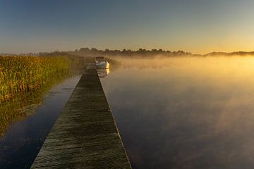 Sunrise on a lake with dew and a boat moored at a jetty in the National Park Weerribben-Wieden, Neth by Dafne Vos