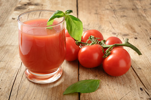 frischer Bio-Tomatensaft im Trinkglas mit Pfeffer und Basilikum garniert auf einem rustikalen Holzbr