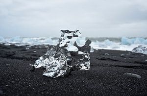 Kristalhelder ijsrots op zwarte sand bij ijsmeer Jokulsarlon, Ijsland
