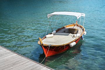 Rode houten boot met ligvlak en zonnescherm op de steiger in het turquoise water van de Middellandse van Maren Winter