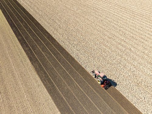 Tractor bewerkt de grond in de lente van bovenaf gezien