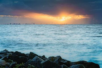 Skyline van Amsterdam met bewolkte zonsondergang met zonnestralen boven het wateroppervlak van de IJsselmeer van Fotografiecor .nl