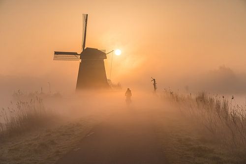 Fietsen door de mist bij een molen op een zonnige ochtend