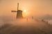 Fietsen door de mist bij een molen op een zonnige ochtend van Jeroen de Jongh