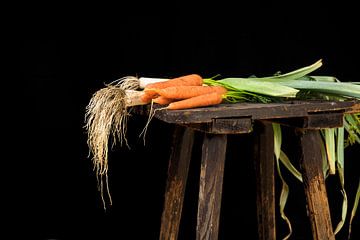 organische Karotten und Lauch, geerntet im Gemüsegarten auf einem alten Holzhocker vor schwarzem Hin von Maren Winter