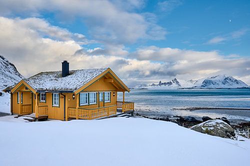 wooden yellow house or hut in winter landscape in stormy weather with sea and mountains