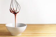 Brown sugar syrup flows from a wire whisk into a white bowl, wooden table and bright background with by Maren Winter thumbnail