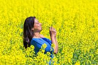 Junge kolumbianische Frau riecht gelbe Blumen in Feld mit landwirtschaftlichen Rapssamen Pflanzen von Ben Schonewille Miniaturansicht