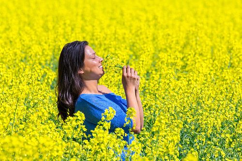 Young colombian woman smelling yellow flowers in agricultural  rapeseed field