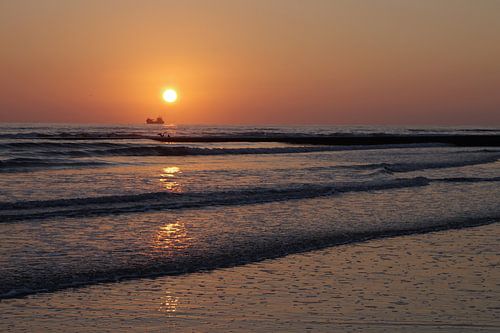 De ondergaande zon wordt weerspiegeld in de golven van de Noordzee