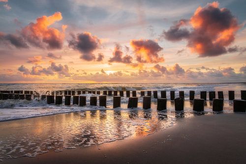Sunset with groynes and colourful clouded sky at Dutch beach