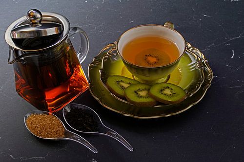 Zwarte thee met kiwi in een kopje, theepot, gesneden kiwi
