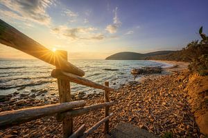 Blick auf den Strand von Cala Violina bei Sonnenuntergang über ein Holzgeländer