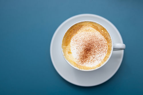Tasse Cappuccino mit Kakaopulver auf blauem Hintergrund, Ansicht direkt von oben, Kopierraum, gewähl