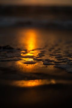 Spiegelung der untergehenden Sonne auf dem Strand mit einer dünnen Wasserschicht