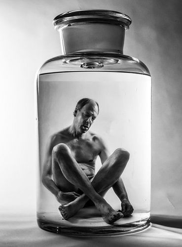 Surrealistisches Schwarz-Weiß-Phantasiebild eines flüssig konservierten Mannes in einem Glas.