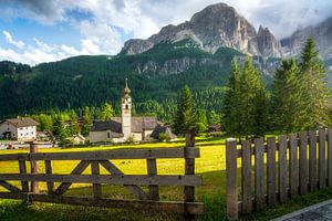 Die Kirche von Colfosco mit Holzzaun und den Dolomiten im Hintergrund, Italien
