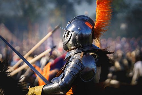 Oranjegezinde ridder in harnas en helm rijdt te paard op historisch slagveld