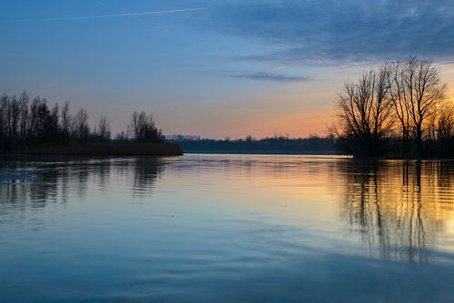 Zonsondergang over een meer met kleine eilandjes aan het eind van een winterdag