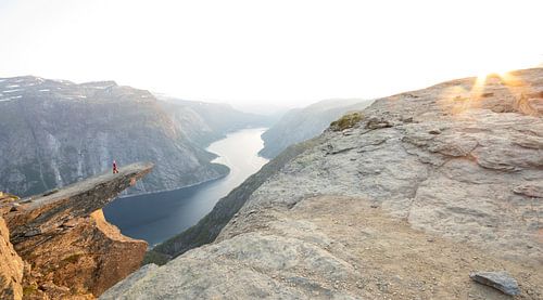 Iemand loopt over de beroemde Trolltunga in Noorwegen bij de laatste zonnestralen