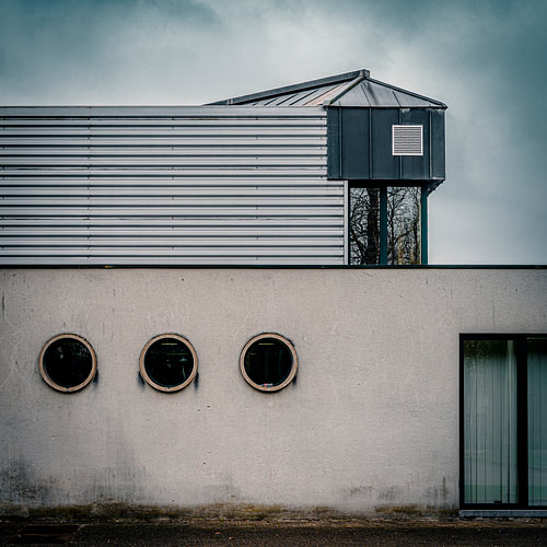 Moderne strakke architectuur met nautische patrijspoorten onder een minimalistische grijze bewolkte lucht