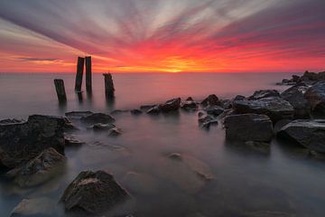 Stenen en palen in het IJsselmeer onder een ochtendrode wolkenlucht van Bram Lubbers