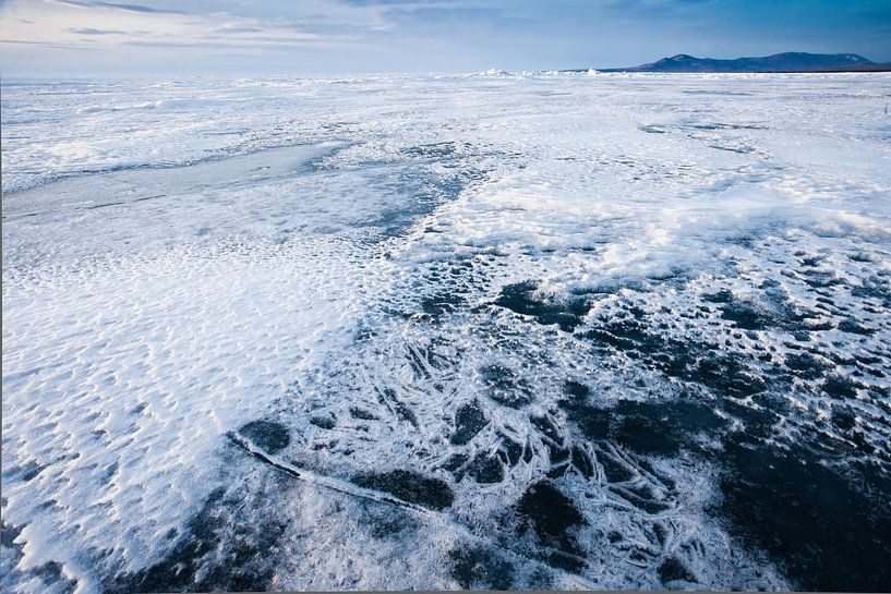 Snow and ice on the flat surface of Lake Baikal under a blue sky in the distance mountain range by Michael Semenov