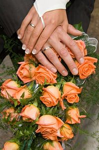 Mains d'un couple de mariés sur le bouquet de la mariée
