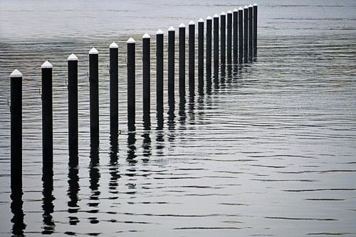 Schwarze Verankerungspfähle oder Dalben aus Beton im Wasser, Ende