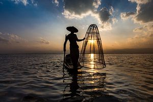 Visser die met traditionele boot op het Inle meer in Myanmar op ouderwetse wijze met een vis korf vi