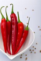 Hot en Spicy, Rode peper in witte stenen schaaltje en losse peper op de witte achtergrond